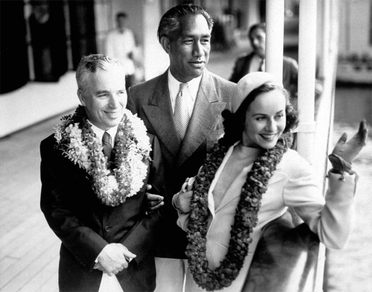 Charlie Chaplin, Duke Kahanamoku e Paulette Goddard a bordo de um navio e acenando para os fãs em 1938 no Havaí.