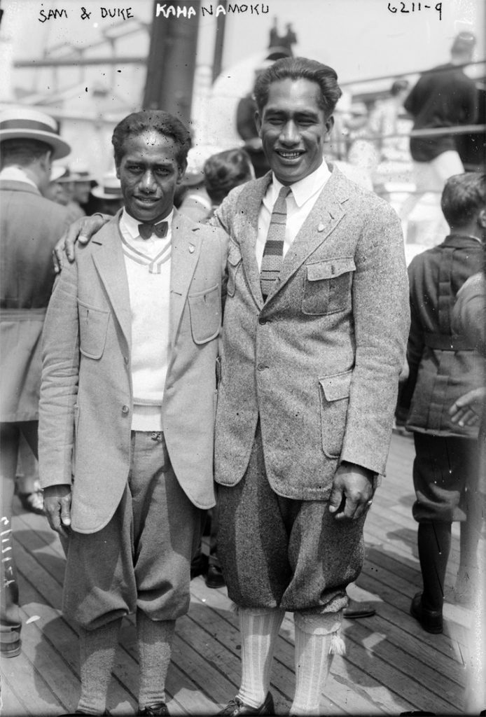 Sam e Duke Kahanamoku sorriem para a câmera a bordo de um transatlântico, por volta de 1920.
